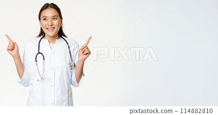 Asian woman doctor in medical uniform and stethoscope, pointing sideways, showing two products, both ways, smiling pleased and looking left, white background Asian woman doctor in medical uniform and stethoscope, pointing sideways, showing two products, both ways, smiling pleased and looking left, white background 114882810