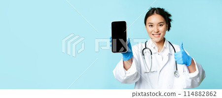Web healthcare, online help concept. Smiling asian female doctor or nurse, showing smartphone screen, app interface and thumbs up, recommending website Web healthcare, online help concept. Smiling asian female doctor or nurse, showing smartphone screen, app interface and thumbs up, recommending website 114882862