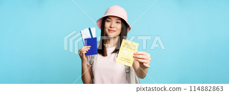 Happy smiling asian tourist, girl shows international vaccination passport, health passport and flight tickets, getting abroad after covid-19 vaccine shot, blue background 114882863