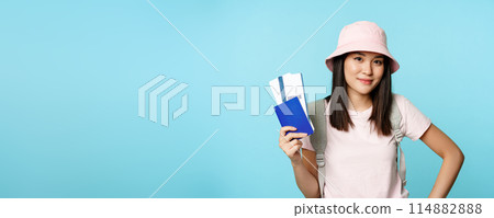 Smiling korean girl tourist, showing passport and tickets for flight, booking hotel, going on trip, voyage, standing over blue background 114882888