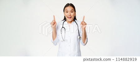 Excited smiling nurse, female doctor in medical uniform pointing up, showing promo sale, healthcare clinic discount, standing over white background 114882919