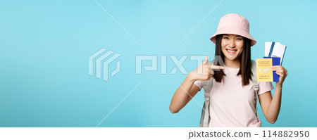 Vaccinated asian tourist, girl showing international health passport, tickets for tour abroad, smiling happy, travelling during covid-19 pandemic, blue background 114882950
