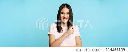 Portrait of happy smiling asian female model, pointing at upper left corner, showing sale banner, store advertisement, blue background 114883169