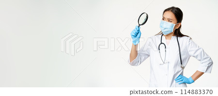 Image of asian female doctor, scientist in medical mask and rubber gloves looks through magnifying glass, searching for smth, white background Image of asian female doctor, scientist in medical mask and rubber gloves looks through magnifying glass, searching for smth, white background 114883370