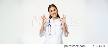 Female smiling doctor, asian healthcare worker in medical clinic uniform shows okay signs, approve smth, give patient permission, stands over white background Female smiling doctor, asian healthcare worker in medical clinic uniform shows okay signs, approve smth, give patient permission, stands over white background 114883391