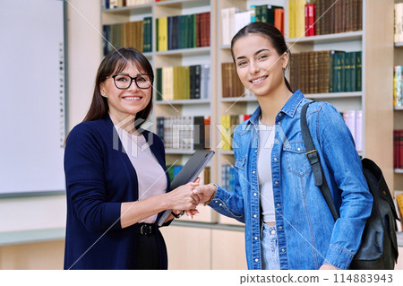 Female teacher shaking hands to teenage girl high school student, inside educational building 114883943