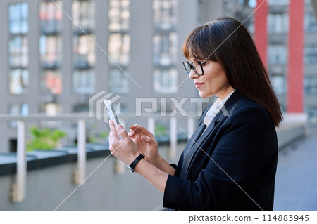 Mature business woman using smartphone, modern city background Mature business woman using smartphone, modern city background 114883945