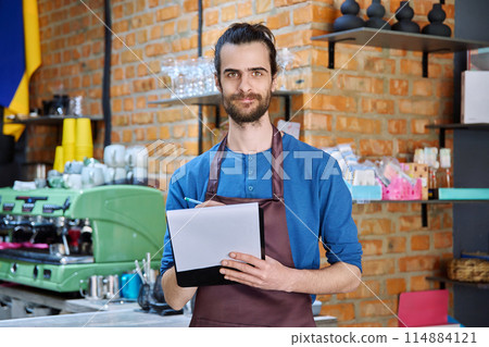Young man in apron, food service worker, small business owner entrepreneur with work papers Young man in apron, food service worker, small business owner entrepreneur with work papers 114884121