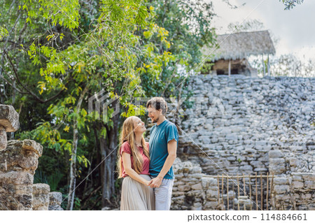 Couple, man and woman tourists at Coba, Mexico. Honeymoon Ancient mayan city in Mexico. Coba is an archaeological area and a famous landmark of Yucatan Peninsula. Cloudy sky over a pyramid in Mexico 114884661