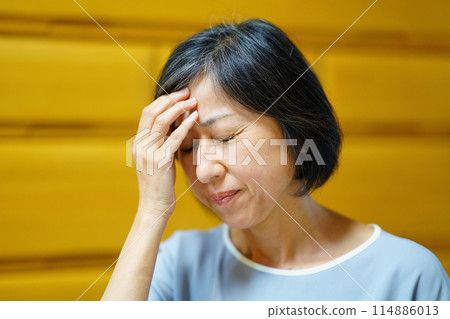 A middle-aged woman complaining of illness with her hand on her forehead 114886013
