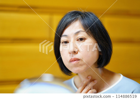 A middle-aged woman looking in the mirror and worrying about her neck A middle-aged woman looking in the mirror and worrying about her neck 114886519