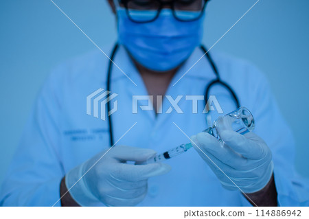 A doctor is holding a syringe and a vial of medicine 114886942