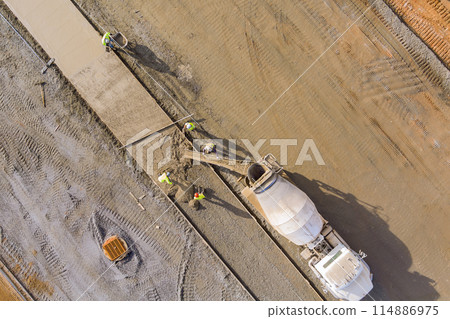 Concrete is poured from mixer truck for construction of pedestrian walkway by masonry workers 114886975
