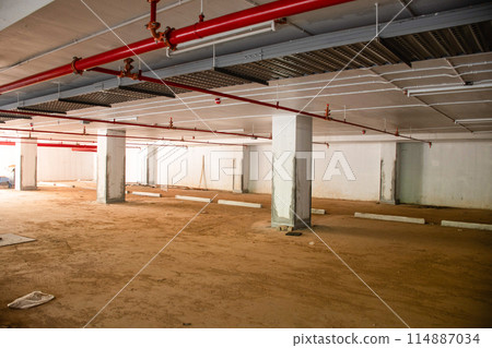 A large empty parking garage with red pipes running through the ceiling A large empty parking garage with red pipes running through the ceiling 114887034