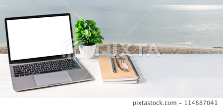 A laptop is on a table next to a plant and a notebook 114887041