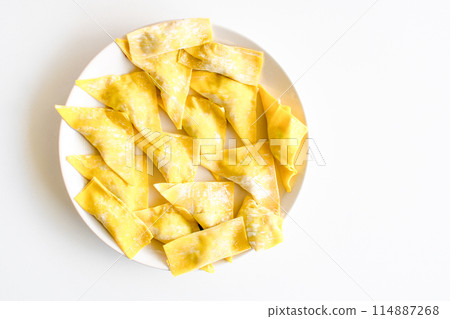 A plate of yellow dumplings sits on a white table A plate of yellow dumplings sits on a white table 114887268