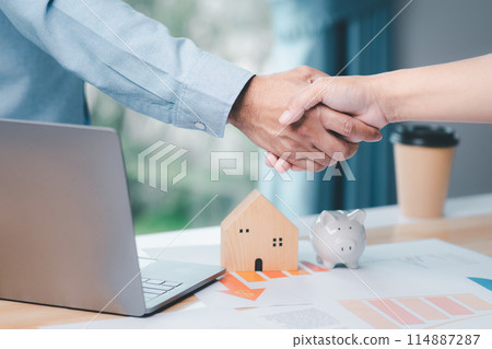 A man shakes hands with another man in front of a laptop and a house model A man shakes hands with another man in front of a laptop and a house model 114887287