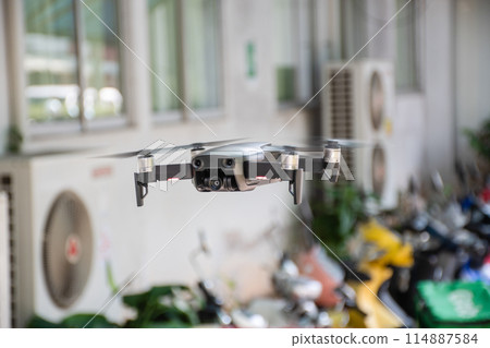 A drone is flying in front of a building with a green sign on the wall 114887584