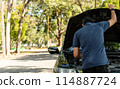 A man is standing next to a car with the hood up 114887724