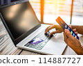 A person is using a laptop and a cell phone to make a purchase 114887727