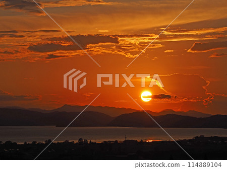 The sun setting on the opposite shore of Lake Inawashiro. The silhouette of the mountain range and the clouds of various shapes floating in the orange sky are impressive and beautiful. The sun setting on the opposite shore of Lake Inawashiro. The silhouette of the mountain range and the clouds of various shapes floating in the orange sky are impressive and beautiful. 114889104
