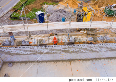 Building working concrete wall with concrete blocks on scaffolding by bricklayer 114889127