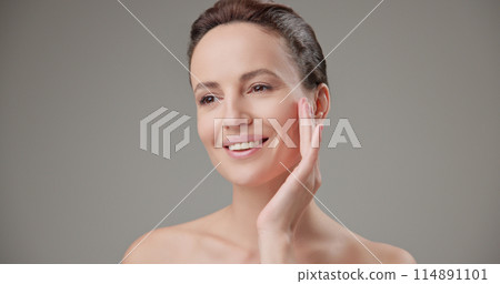 Beauty, health, cosmetics, anti-aging therapy and skin care concept - young beautiful brunette Caucasian woman touching face and looking at camera smiling 114891101