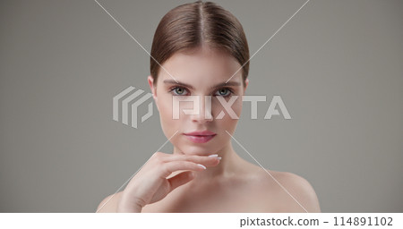Beauty, health, cosmetics, anti-aging therapy and skin care concept - young beautiful brunette Caucasian woman touching face and looking at camera 114891102