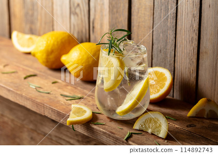 Summer refreshing drink with ice, rosemary and lemon slices on a old wooden table. 114892743