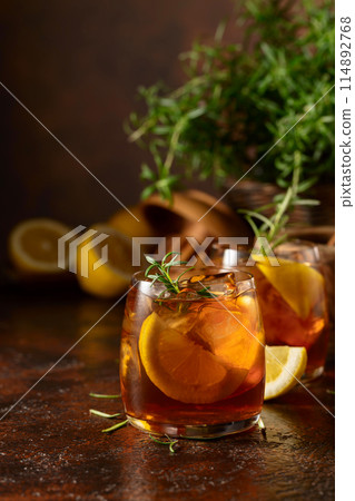 Iced tea or cocktail with ice, rosemary and lemon slices on the old brown table. Iced tea or cocktail with ice, rosemary and lemon slices on the old brown table. 114892768