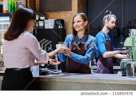 Woman customer of coffee shop near counter with cup of coffee talking to restaurant workers 114893476