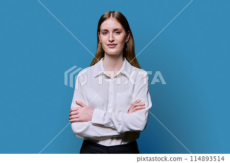 Portrait of teenage smiling female in white shirt with crossed arms on blue background Portrait of teenage smiling female in white shirt with crossed arms on blue background 114893514