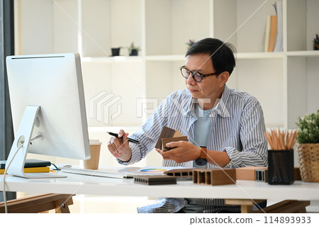 Experienced interior designer working on project comparing samples of materials at office 114893933