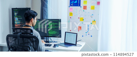 Asian software developers working on multiple screens displaying code and application diagrams in a modern office 114894527