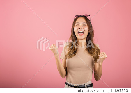 Happy Asian portrait beautiful cute young woman wear glasses makes raised hand up celebrating her winning success gesture, studio shot isolated pink background, Female excited say yes with copy space 114895220