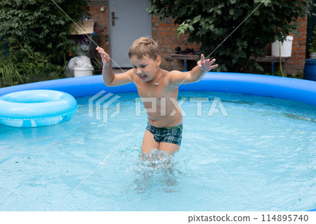 In the summer, a boy child with his eyes closed jumps into the water in the pool and raises a lot of splashes. A child loves to swim in the pool in the yard of his house on a hot summer day. 114895740