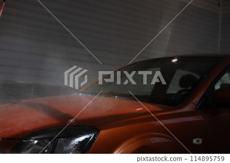 In a car wash, a man washes his car with water in a box. Washing a car with a high pressure water gun. Car wash service. In a car wash, a man washes his car with water in a box. Washing a car with a high pressure water gun. Car wash service. 114895759