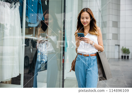 Woman with a smartphone in her hand, standing in front of a wall. She is using her device to stay connected to the digital age, enjoying the entertainment and distraction it offers. Woman with a smartphone in her hand, standing in front of a wall. She is using her device to stay connected to the digital age, enjoying the entertainment and distraction it offers. 114896109