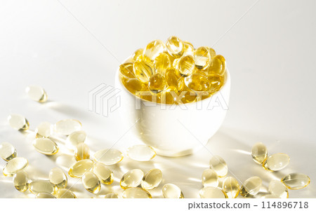 Transparent yellow vitamins on a light background. Vitamin D, omega 3, omega 6, Food supplement oil filled fish oil, vitamin A, vitamin E, flaxseed oil. Transparent yellow vitamins on a light background. Vitamin D, omega 3, omega 6, Food supplement oil filled fish oil, vitamin A, vitamin E, flaxseed oil. 114896718