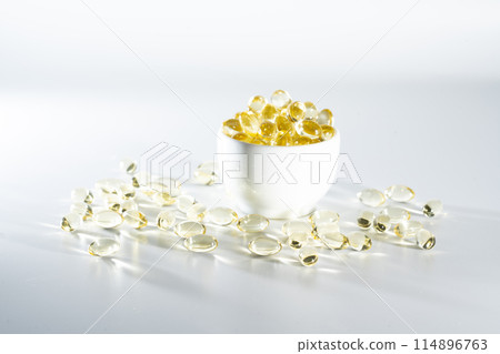 Transparent yellow vitamins on a light background. Vitamin D, omega 3, omega 6, Food supplement oil filled fish oil, vitamin A, vitamin E, flaxseed oil. Transparent yellow vitamins on a light background. Vitamin D, omega 3, omega 6, Food supplement oil filled fish oil, vitamin A, vitamin E, flaxseed oil. 114896763