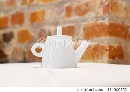 White teapot on table with brick wall background 114900752