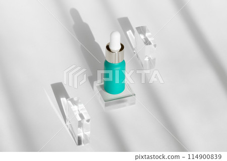 teal serum bottle surrounded by crystal blocks casting elegant shadows on white background 114900839