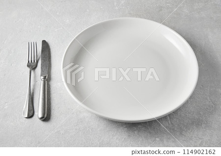 White ceramic plate with knife and fork on a gray stone table. Template for displaying food on the menu 114902162