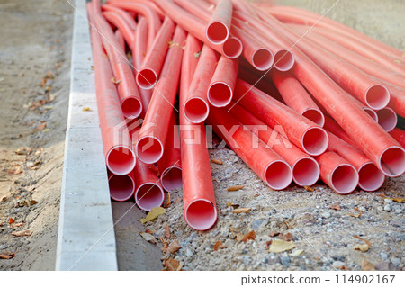 Pile of plastic red water pipes at a construction site. Laying utility lines under the road surface Pile of plastic red water pipes at a construction site. Laying utility lines under the road surface 114902167