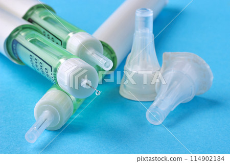 Closeup of a drop of medicine on the tip of a pen syringe needle. Insulin syringes and needles on blue background Closeup of a drop of medicine on the tip of a pen syringe needle. Insulin syringes and needles on blue background 114902184