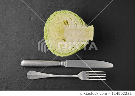 White cabbage in a cut, fork and knife on a black stone tabletop White cabbage in a cut, fork and knife on a black stone tabletop 114902221