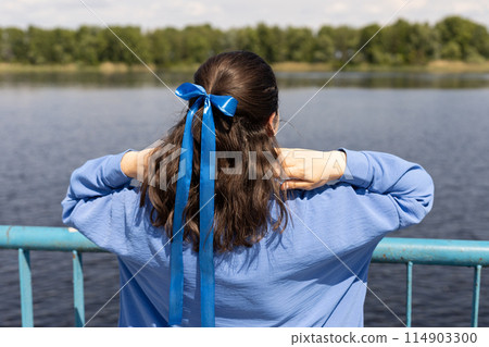 young woman with a blue bow is looking at the pond, back view young woman with a blue bow is looking at the pond, back view 114903300
