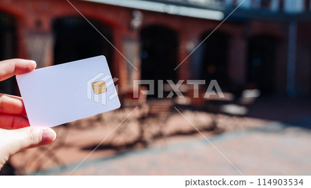 A person is holding a white credit card with a gold chip A person is holding a white credit card with a gold chip 114903534