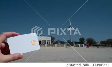A person holding a credit card in front of a wind turbine A person holding a credit card in front of a wind turbine 114903542