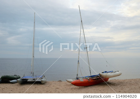 Catamarans with masts on lake shore. 114904020